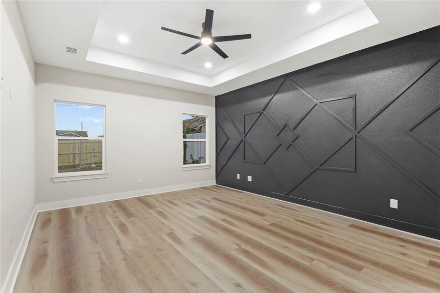 Spare room featuring an accent wall, light wood finished floors, a tray ceiling, ceiling fan, and recessed lighting
