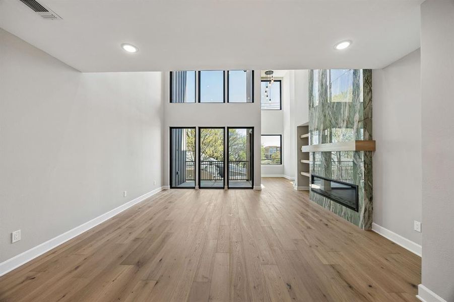 Unfurnished living room with a fireplace, a high ceiling, light wood finished floors, recessed lighting, and built in shelves Unfurnished living room with a fireplace, a high ceiling, light wood finished floors, recessed lighting, and built in shelves
