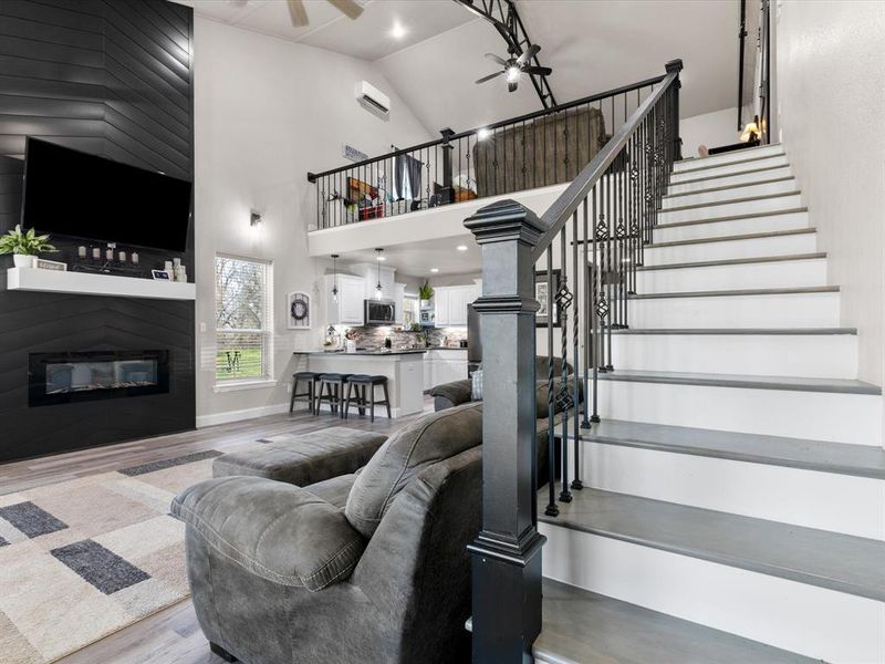 Living area featuring stairway, wood finished floors, high vaulted ceiling, ceiling fan, and a glass covered fireplace