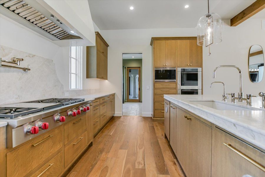 Kitchen featuring stainless steel appliances, light wood-type flooring, wood finish cabinetry, beam ceiling, and decorative light fixtures