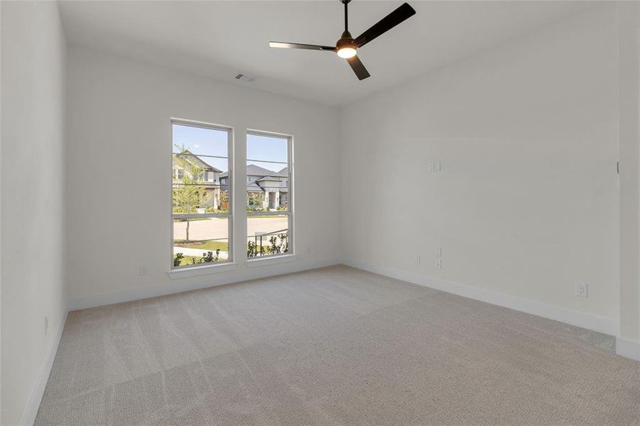 Bright interior room featuring a modern ceiling fan, two large windows, soft carpet flooring, and crisp white walls