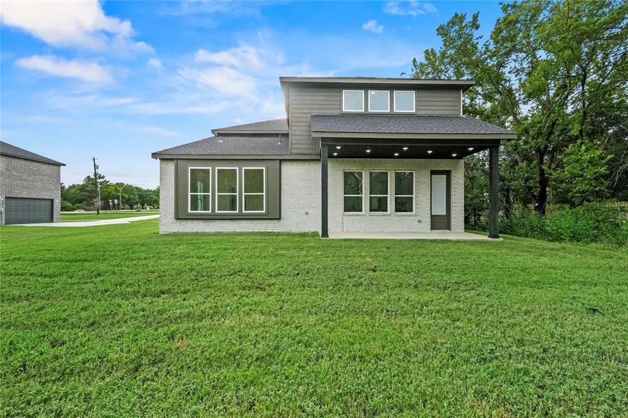 Rear view of house featuring a patio, a lawn, a shingled roof, and brick siding Rear view of house featuring a patio, a lawn, a shingled roof, and brick siding