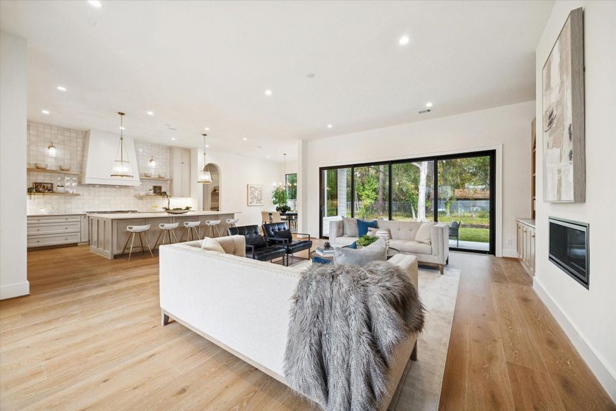 Expansive open living area with white oak wood floors, modern fireplace, and sliding doors to the backyard.