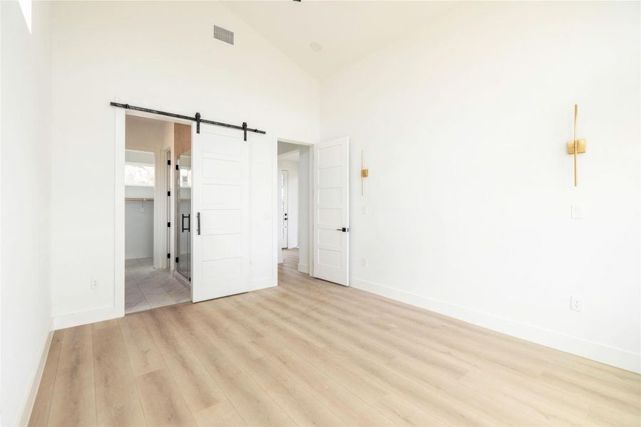 Unfurnished bedroom featuring a barn door, light wood finished floors, lofted ceiling, connected bathroom, and a spacious closet