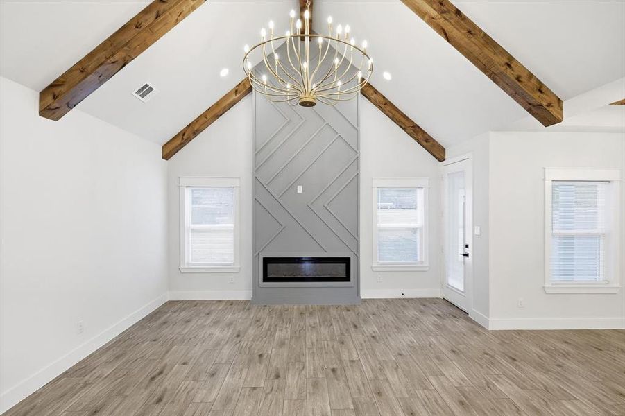 Unfurnished living room with plenty of natural light, a large fireplace, light wood finished floors, a chandelier, and beam ceiling