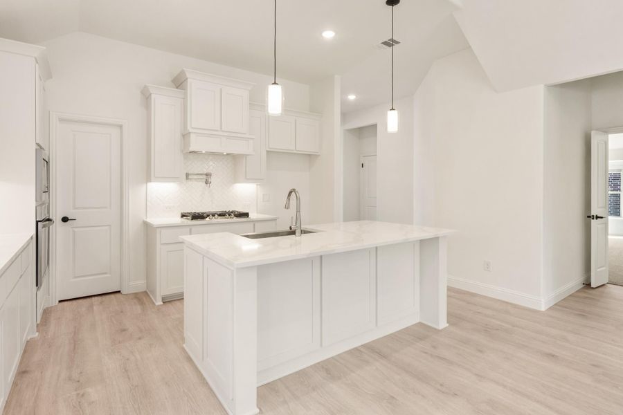White kitchen with center island, sink, pendant lights, white cabinets, and light wood floors