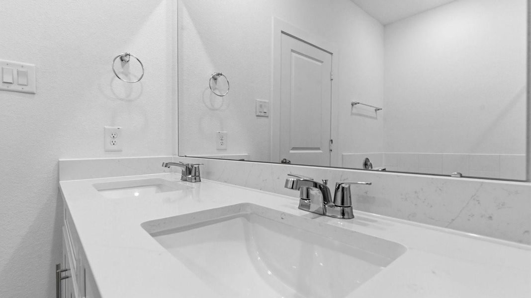 Modern primary bathroom with double vanities, quartz countertops, and a glass-enclosed shower with a walk-in closet.