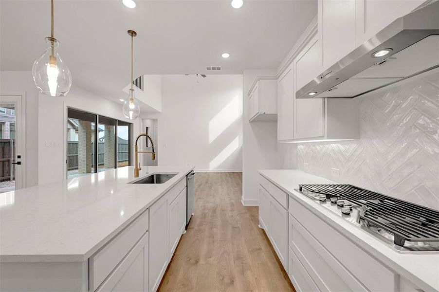 Kitchen with white cabinets, a large island with sink, stainless steel appliances, light wood-type flooring, and hanging light fixtures