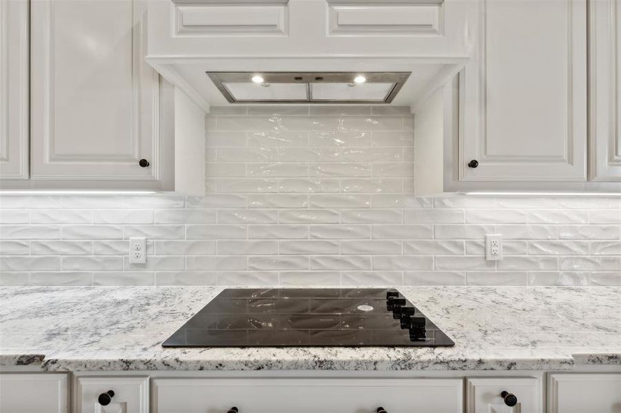 Kitchen featuring light stone countertops, white cabinetry, tasteful backsplash, and black electric cooktop