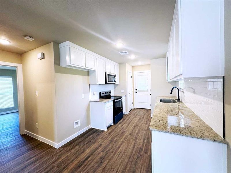 Kitchen featuring dark wood-style floors, visible vents, a sink, stainless steel microwave, and black electric range