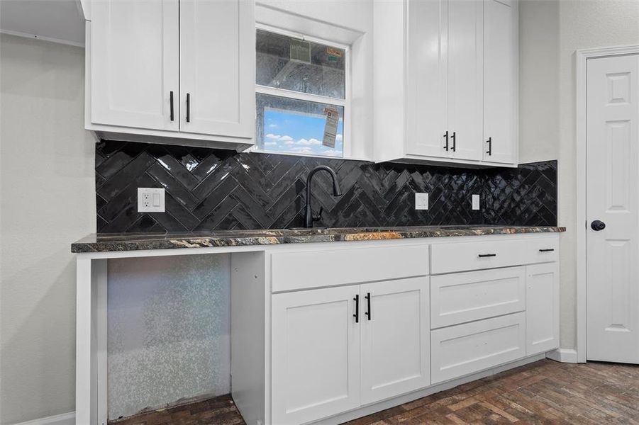 Kitchen with decorative backsplash, dark stone counters, white cabinets, and brick floors Kitchen with decorative backsplash, dark stone counters, white cabinets, and brick floors