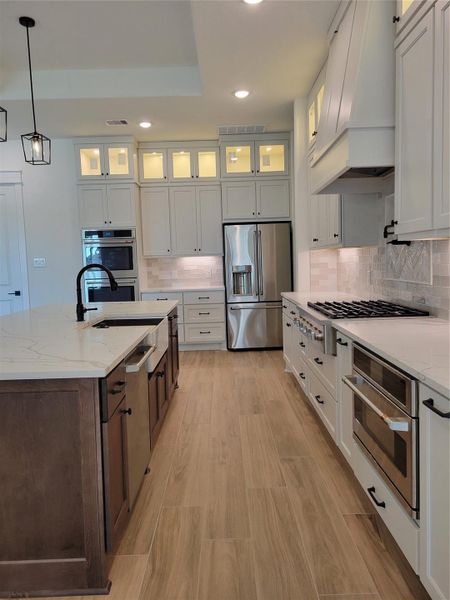 This modern kitchen features sleek stainless steel CAFE appliances, a spacious island with a dark wood base, and elegant custom white cabinetry with glass accents. It includes a gas cooktop, built-in oven, and ample counter space, all highlighted by stylish lighting and light wood flooring. This modern kitchen features sleek stainless steel CAFE appliances, a spacious island with a dark wood base, and elegant custom white cabinetry with glass accents. It includes a gas cooktop, built-in oven, and ample counter space, all highlighted by stylish lighting and light wood flooring.