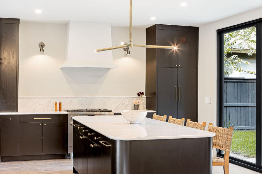 Kitchen featuring stainless steel gas range oven, light stone counters, a center island, a kitchen bar, and light wood-style flooring Kitchen featuring stainless steel gas range oven, light stone counters, a center island, a kitchen bar, and light wood-style flooring