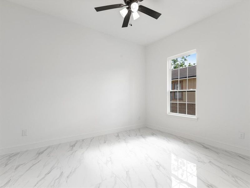 Spare room featuring marble look tiles, a ceiling fan, and baseboards
