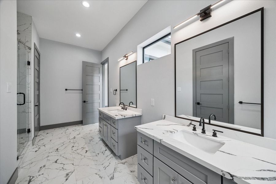 Dual sinks, and generous cabinet storage make the bathroom both stylish and practical. Marble-look flooring and counters complete the modern aesthetic, perfect for everyday living.