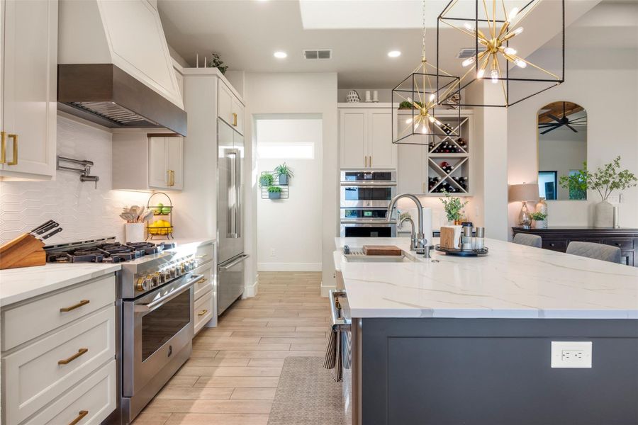 Kitchen with custom exhaust hood, hanging light fixtures, high quality appliances, light stone countertops, and white cabinets Kitchen with custom exhaust hood, hanging light fixtures, high quality appliances, light stone countertops, and white cabinets