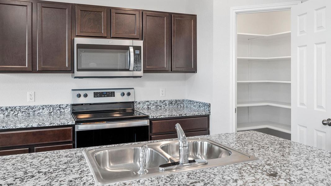 Kitchen featuring dark wood finish cabinets, stainless steel appliances, and light stone countertops