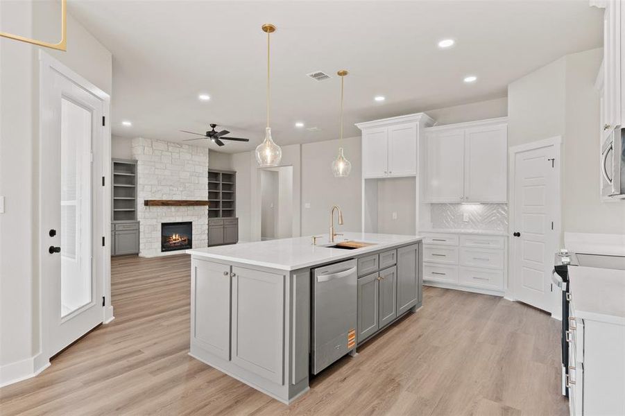 Kitchen featuring a stone fireplace, a center island with sink, decorative light fixtures, light wood-type flooring, and two tone cabinets