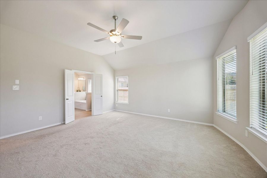This photo of the primary bedroom shows a glimpse of the en suite bathroom as well as the ceiling fan for easy sleeping.