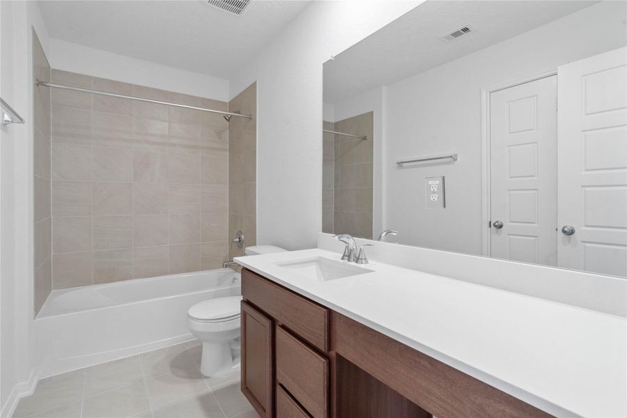 The secondary bathroom offers tile flooring, a bath/shower combination with a stylish tile surround, rich stained wood cabinetry with added knee space and elegant light countertops, a mirror, and sleek fixtures with modern finishes. The secondary bathroom offers tile flooring, a bath/shower combination with a stylish tile surround, rich stained wood cabinetry with added knee space and elegant light countertops, a mirror, and sleek fixtures with modern finishes.