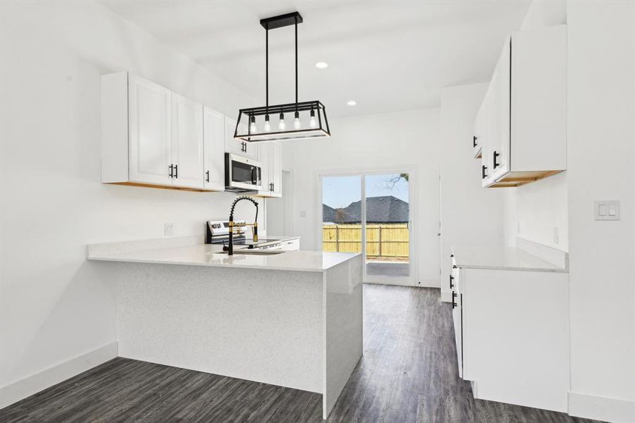 Kitchen featuring dark wood-style floors, stainless steel appliances, a peninsula, and light countertops