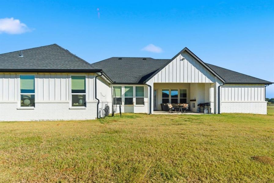 Back of house featuring board and batten siding, a patio, and a yard