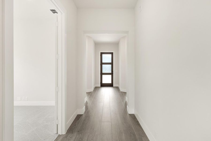 Hallway with white walls, dark wood floors, and glass-panel door at the end