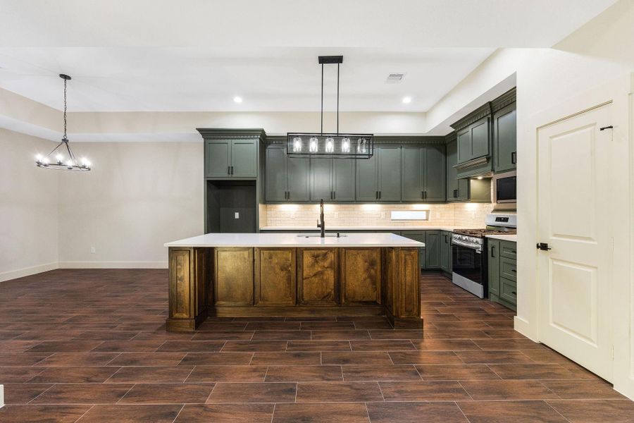 This modern kitchen with dark green cabinetry, a spacious island with a wooden base, and sleek appliances. The open layout features wood-look tile flooring and contemporary lighting, providing a warm and inviting atmosphere.