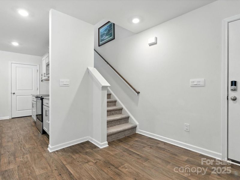Open staircase with carpeted steps and handrail leads to upper level. Clean white walls, luxury vinyl plank flooring, and thoughtful layout create welcoming entry space with excellent flow throughout the home.