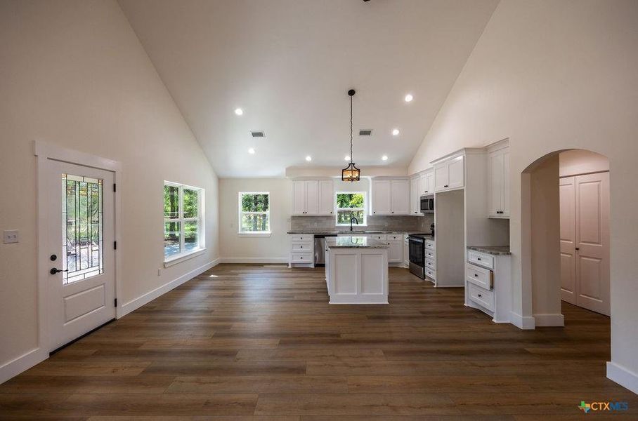 Kitchen with arched walkways, high vaulted ceiling, a center island, white cabinets, and decorative light fixtures