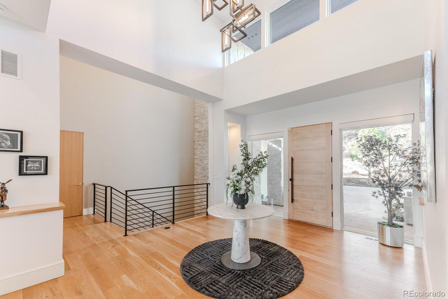 A grand two-story entry and modern door flanked by full-height glass invites light to pour across wide white-oak floors that extend uninterrupted throughout the main level.