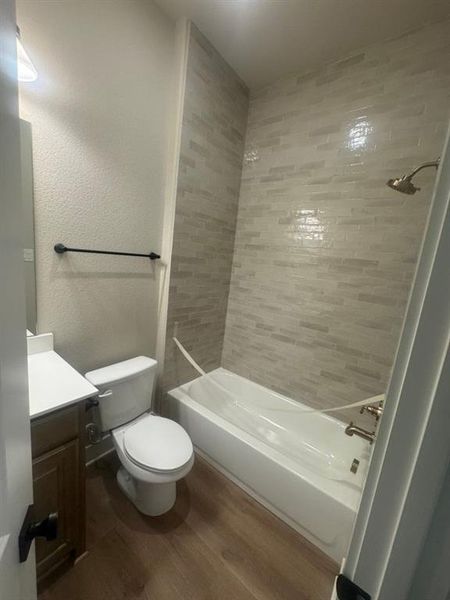 Bathroom featuring a white bathtub, tiled shower surround, light wood-finish flooring, and a vanity with a white countertop