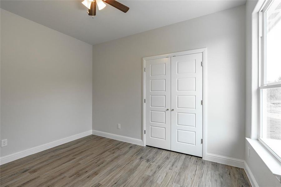 Unfurnished bedroom with ceiling fan, a closet, light wood-type flooring, and multiple windows