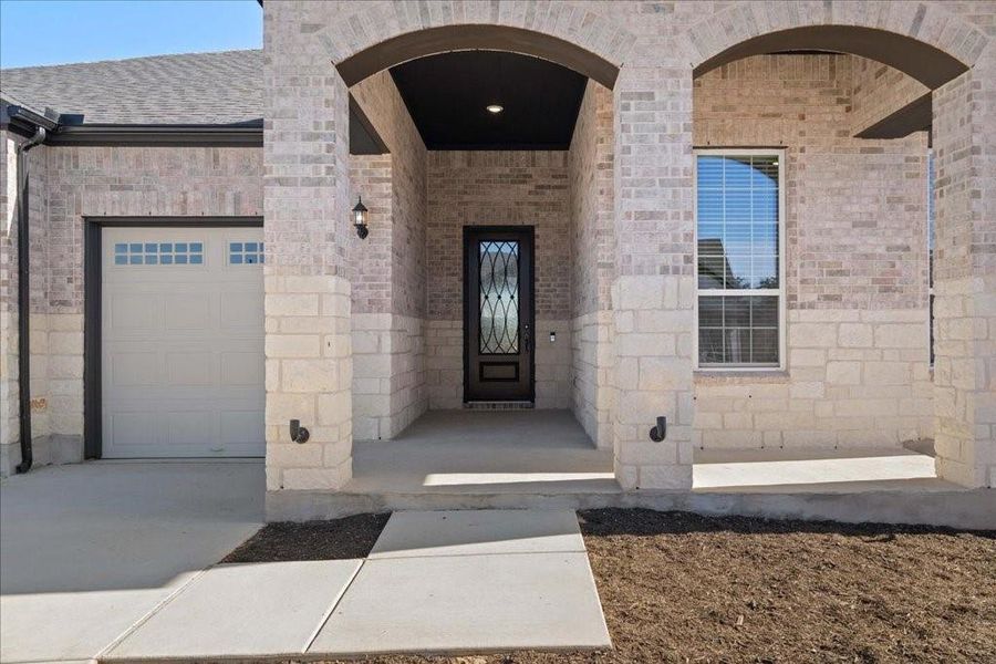 Spacious front entryway surrounded by a brick and stone exterior with upgraded uplighting.