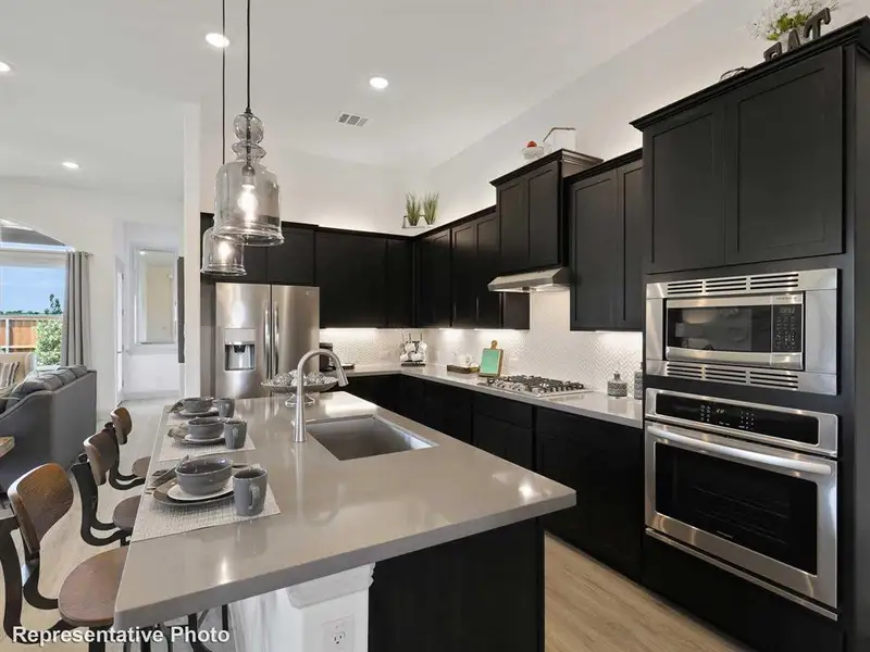 Spacious kitchen featuring dark cabinetry, stainless steel appliances, an island with a sink, and pendant lighting