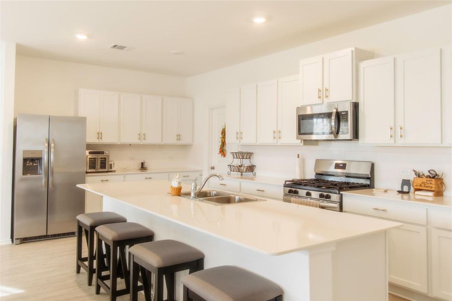 Gourmet kitchen with stainless steel appliances, elegant white cabinetry, light wood-inspired flooring, quartz countertops, and a beautifully detailed backsplash—perfect for cooking and entertaining.