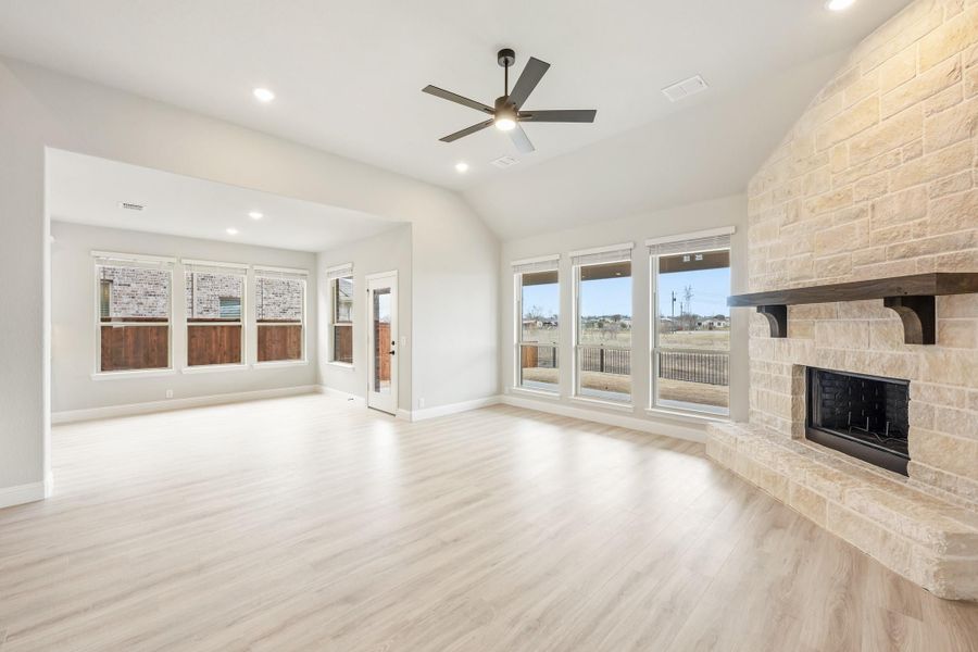 Open living room with stone fireplace, vaulted ceiling, ceiling fan, and light hardwood floors Open living room with stone fireplace, vaulted ceiling, ceiling fan, and light hardwood floors
