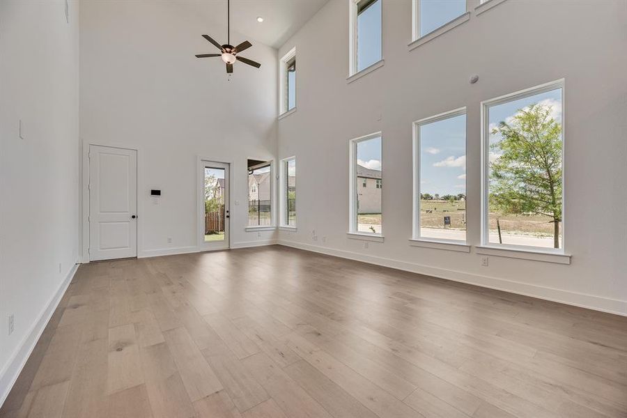 Unfurnished living room with light wood-type flooring, healthy amount of natural light, a high ceiling, and ceiling fan Unfurnished living room with light wood-type flooring, healthy amount of natural light, a high ceiling, and ceiling fan