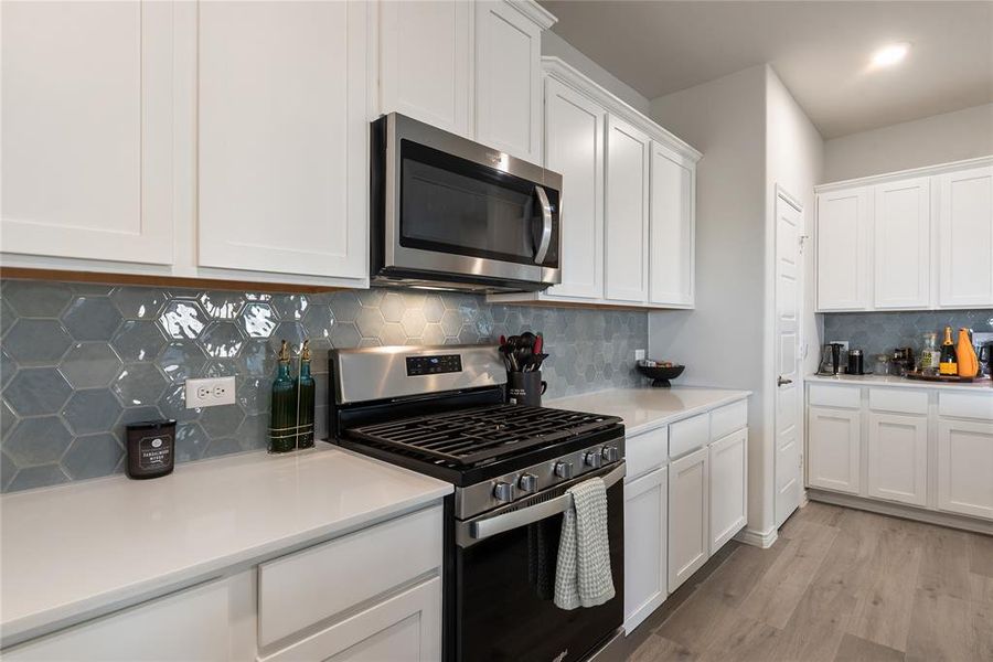 Kitchen featuring stainless steel appliances, tasteful backsplash, white cabinetry, light wood-style floors, and light stone counters