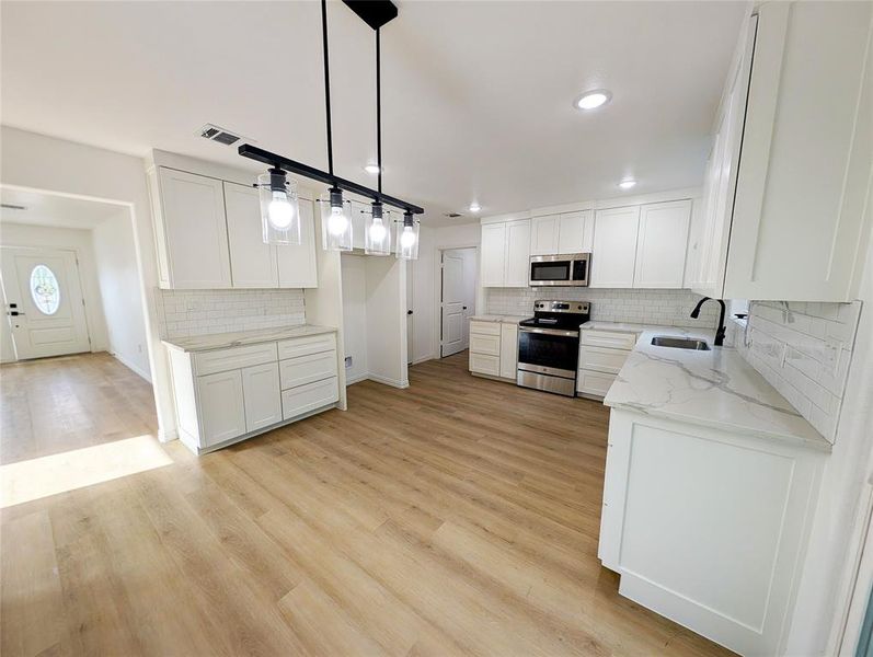 Kitchen with pendant lighting, appliances with stainless steel finishes, white cabinetry, sink, and light stone counters