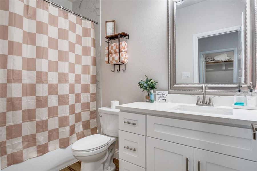 Bathroom with vanity, shower / bathtub combination with curtain, and a textured wall