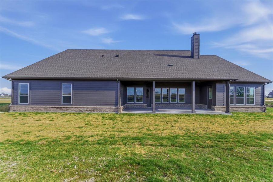 Back of house featuring a patio, a lawn, and a shingled roof