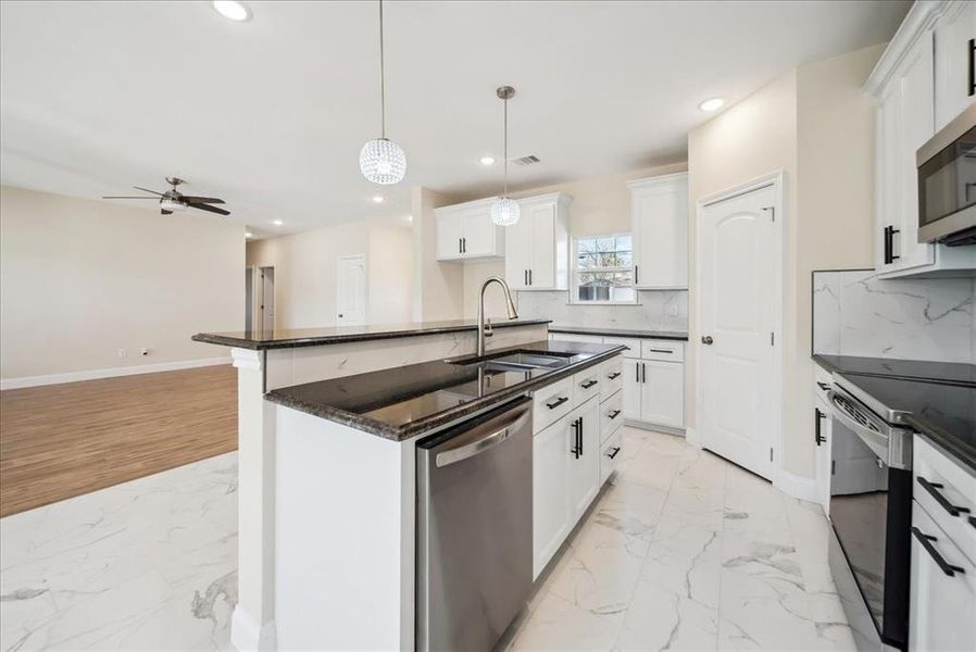 Kitchen with appliances with stainless steel finishes, a kitchen island with sink, sink, white cabinetry, and hanging light fixtures