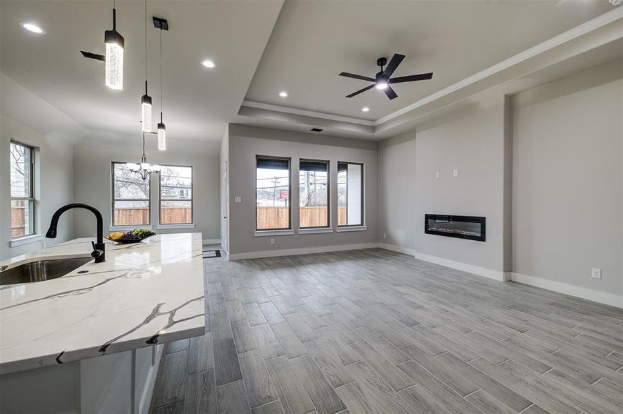 Unfurnished living room featuring a healthy amount of sunlight, sink, light wood-type flooring, and a tray ceiling