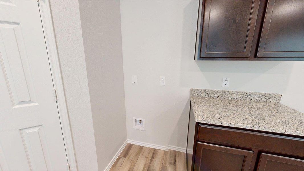Utility area featuring wood-finish flooring, dark wood cabinetry, and a light speckled countertop Utility area featuring wood-finish flooring, dark wood cabinetry, and a light speckled countertop
