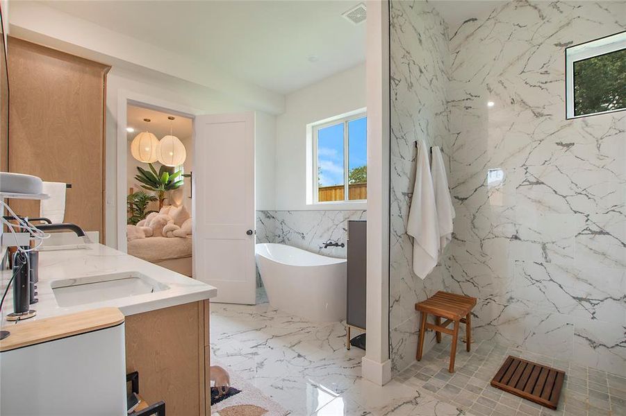 Bathroom with tile walls, light marble finish floors, double vanity, stone wall, and a freestanding tub Bathroom with tile walls, light marble finish floors, double vanity, stone wall, and a freestanding tub