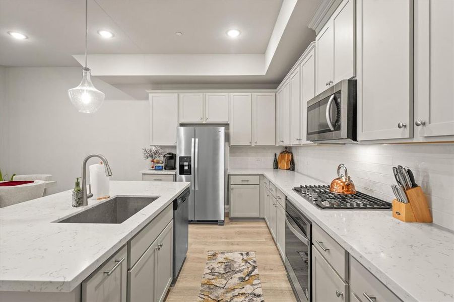 Kitchen with light hardwood / wood-style flooring, stainless steel appliances, light stone countertops, decorative light fixtures, and sink