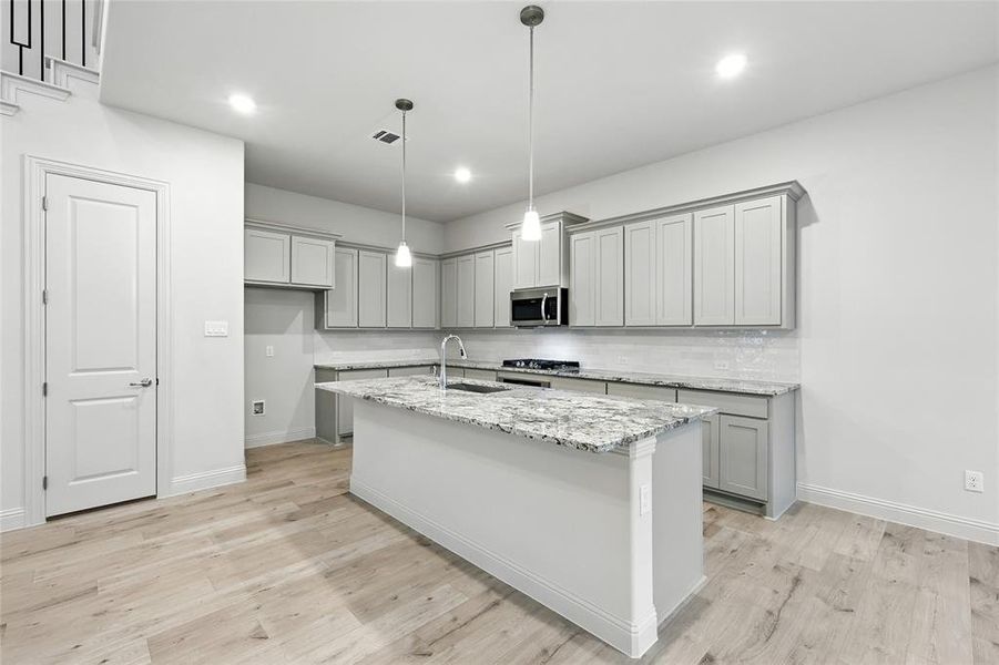 Kitchen featuring gray cabinets, hanging light fixtures, light stone countertops, light wood-type flooring, and recessed lighting