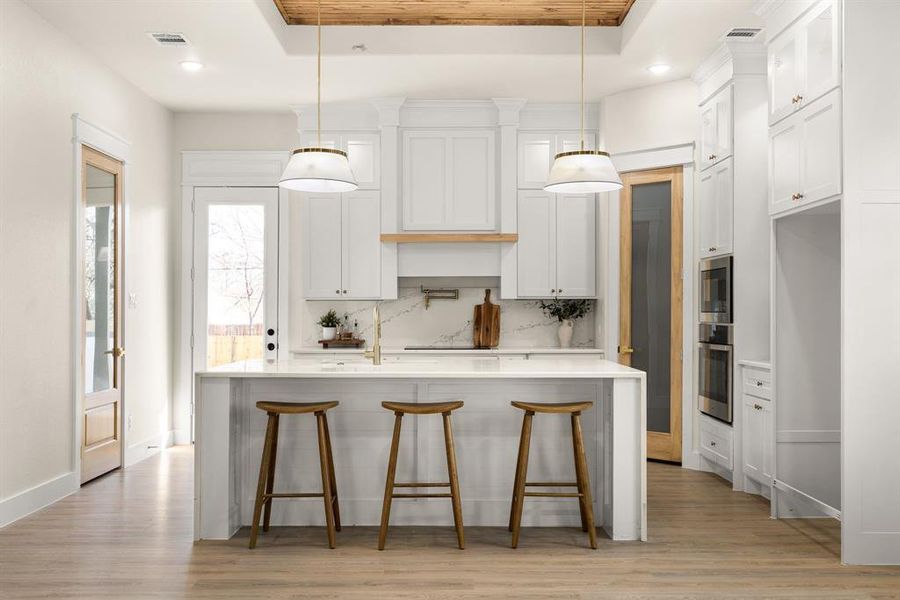 Kitchen with tasteful backsplash, white cabinetry, a raised ceiling, and light countertops