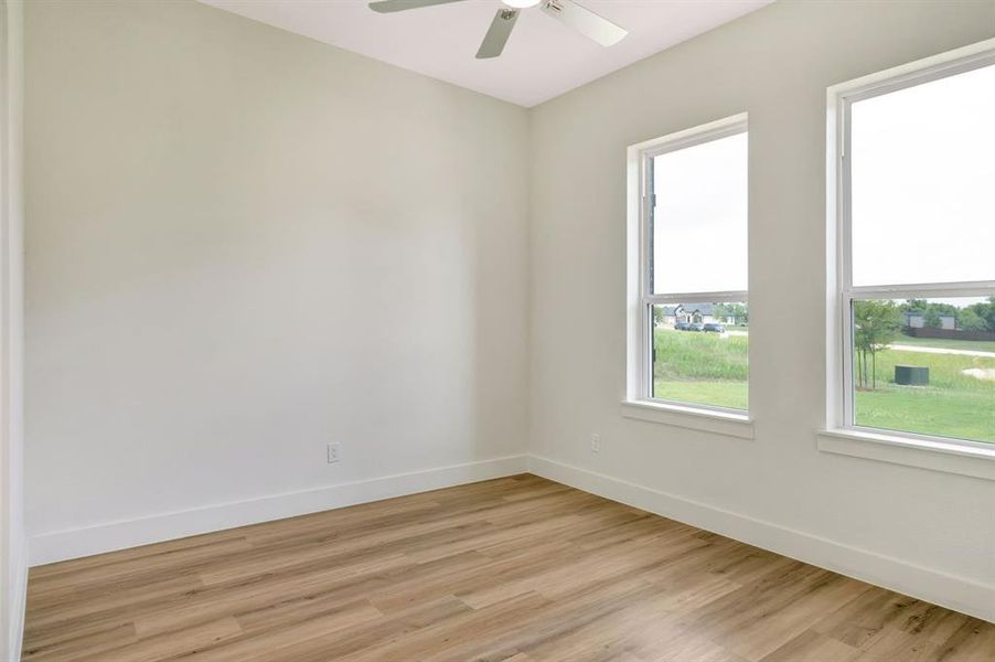 Room featuring two large windows, wood-finish flooring, a ceiling fan, and white baseboards Room featuring two large windows, wood-finish flooring, a ceiling fan, and white baseboards